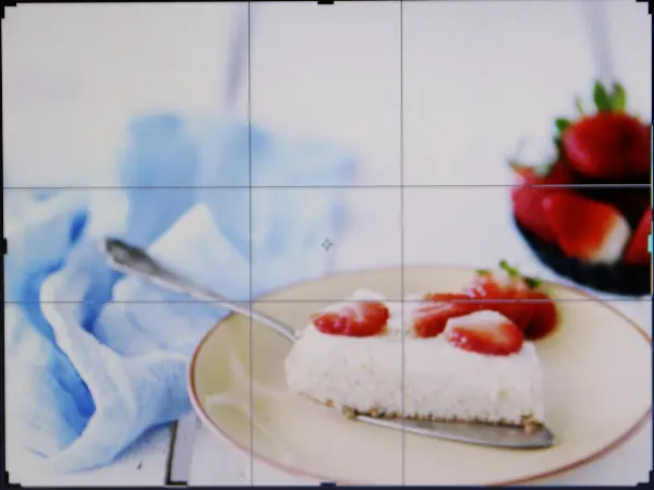 Ein Dessertteller mit einem Stück Kuchen, garniert mit Erdbeeren, auf einem weißen Tisch vor einem blauen Tuch.