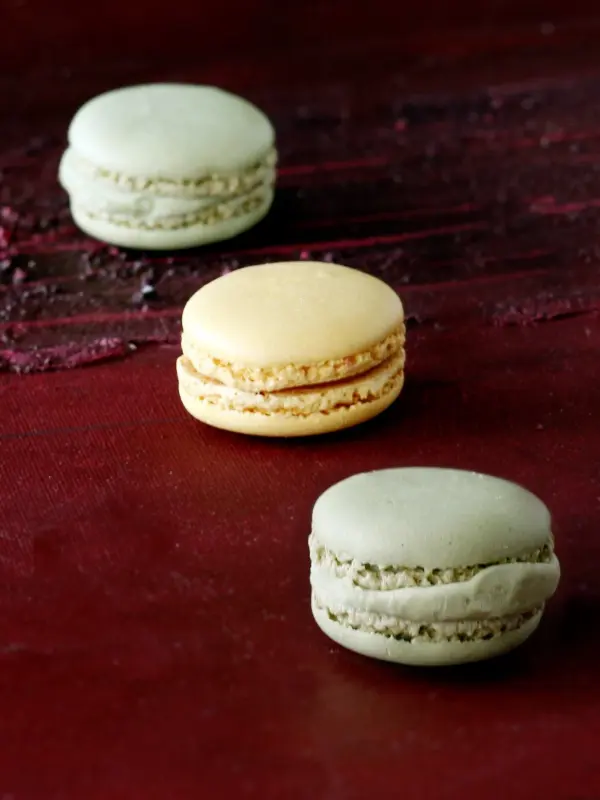 Drei farbige Macarons liegen auf einer dunklen Oberfläche, bereit für ein Rezept oder als Fotomotiv für bessere Fotos.