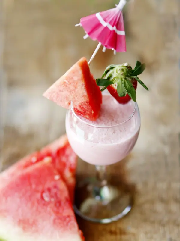 Ein erfrischender Wassermelonensmoothie in einem eleganten Glas mit einer kleinen Schirmchen-Dekoration steht auf einem Holztisch.