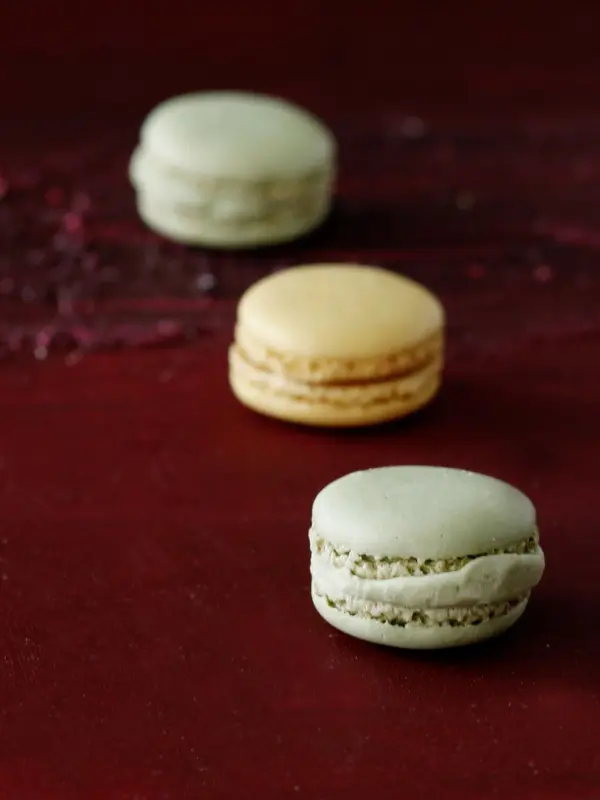 Drei farbige Macarons liegen auf einer roten Hintergrundfläche, bereit für eine ansprechende Rezeptdarstellung.