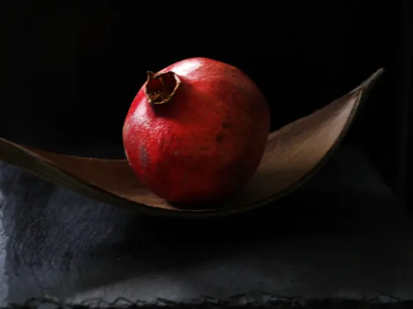 Eine Granatapfel sitzt auf einer eleganten Schale und wird von einem dunklen Hintergrund hervorgehoben, ideal für Rezeptfotos.