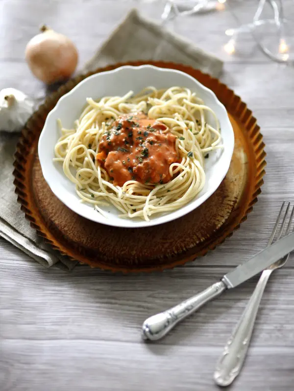 Ein Teller mit Spaghetti in Tomatensauce liegt auf einem dekorativen Teller, umgeben von Besteck und einer sanften Tischumgebung.