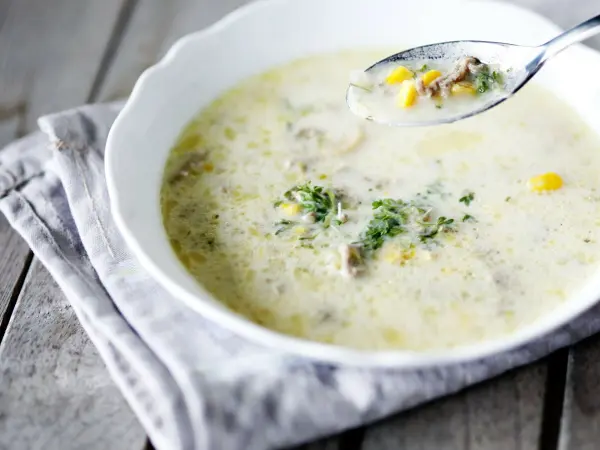 Eine schmackhafte Suppe mit Kräutern wird mit einem Löffel aufgenommen. Der Teller steht auf einem rustikalen Holztisch.