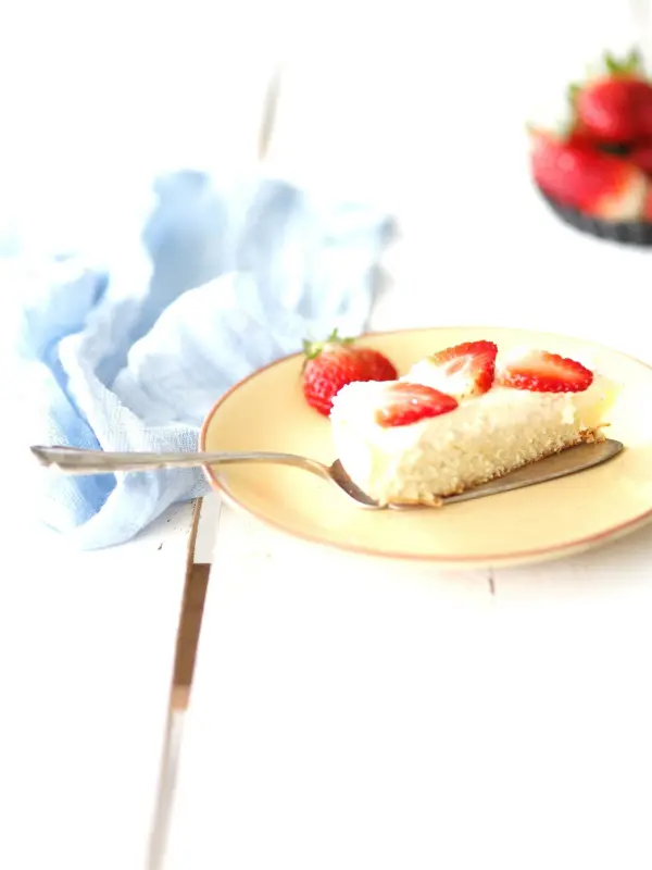 Ein Stück Kuchen mit Erdbeeren liegt auf einem gelben Teller, während eine Gabel daneben auf einem weißen Tisch ruht.