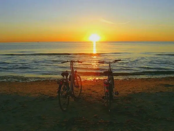 Zwei Fahrräder stehen am Strand und beobachten den Sonnenuntergang über dem ruhigen Meer, ideal für Ausflüge ins Grüne.