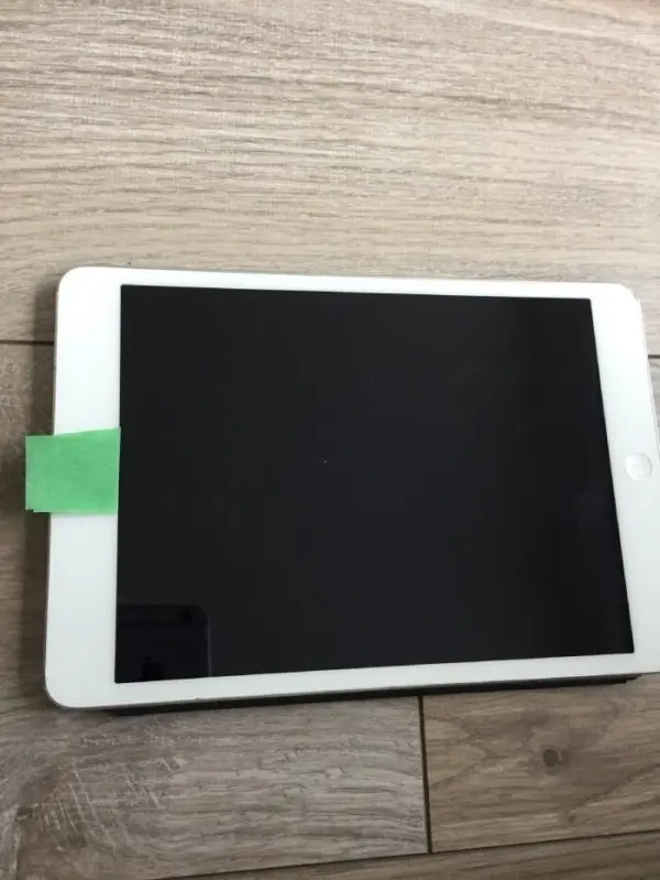 Ein Tablet liegt auf einem Holztisch, es hat ein grünes Klebeband auf der oberen Kante zum Schutz vor Kamera-Überwachung.