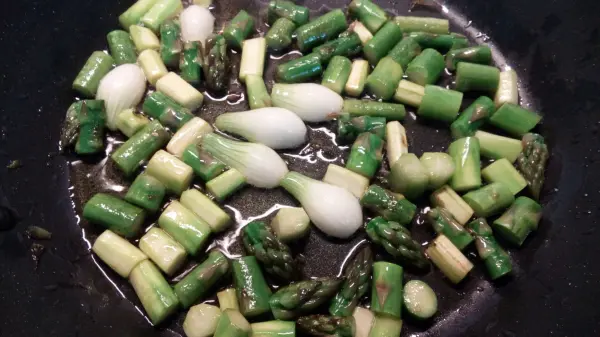 Grüner Spargel und Rhabarberstücke braten in einer Pfanne, um einen frischen Salat zuzubereiten. Ein leuchtendes Gericht.