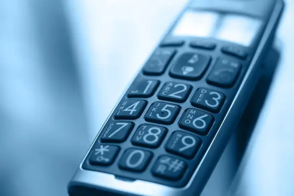 Ein Telefon mit Tasten liegt auf einem Tisch, während es zum Wählen bereit ist, im Kontext einer ruhigen Umgebung.