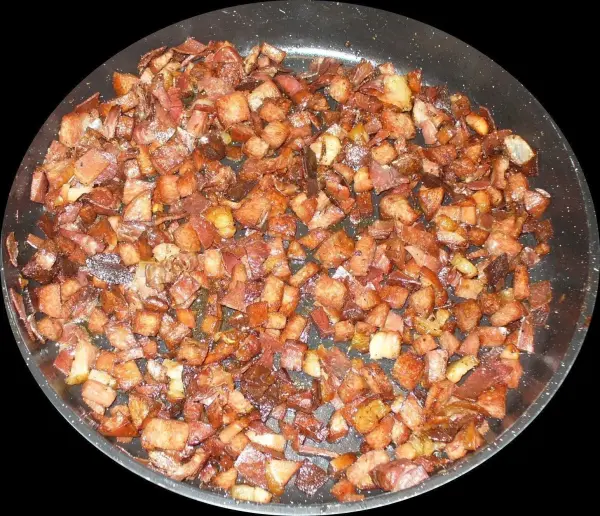 Kleine Stücke gebratener Speck liegen in einer Pfanne und sind bereit für das schnelle Rührei in der Küche.
