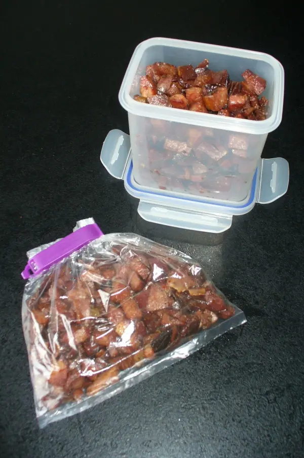 Kleine Stücke von Speck in Behältern, die zum Einfrieren vorbereitet sind, auf einer dunklen Oberfläche.
