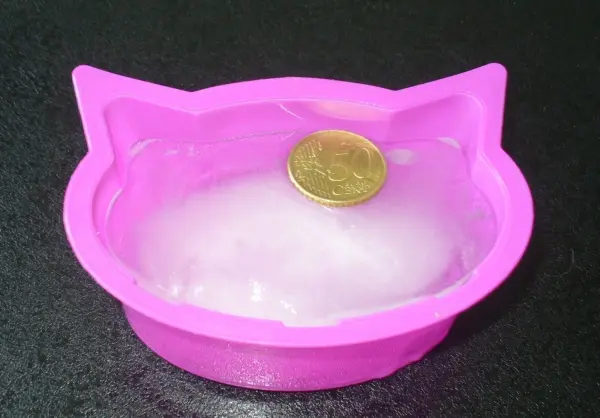 Eine pinke Schale in Katzenform, die einen Euro zeigt, steht auf einer dunklen Oberfläche und deutet auf etwas Lustiges hin.