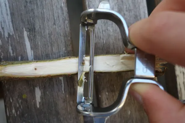 Ein Handwerker verwendet einen Schäler, um einen Stock für Kräuterschilder vorzubereiten, auf einem Holzuntergrund.