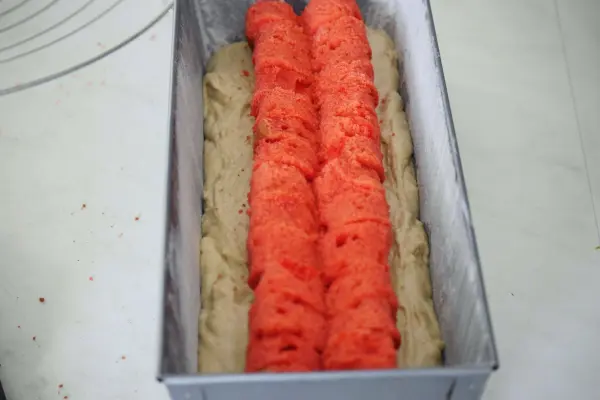 Ein Rührkuchen mit roten Herzen wird in einer Kastenform vorbereitet, umgeben von hellem Teig.