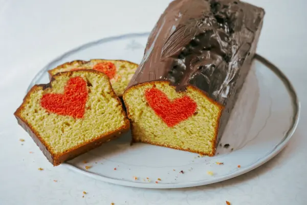 Der saftige Rührkuchen mit Herzen wird auf einem Teller präsentiert, mit einer Schokoladenglasur und roten Herzmuster im Inneren.