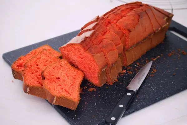 Ein farbenfroher Rührkuchen mit Herz wird auf einem schwarzen Brett geschnitten, neben einem Messer liegt.