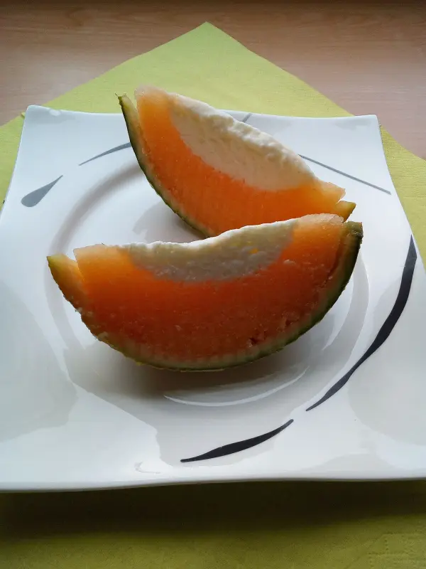 Zwei halbe Melonenstücke liegen auf einem weißen Teller. Die orangefarbene Frucht hat einen cremigen Joghurtkern.