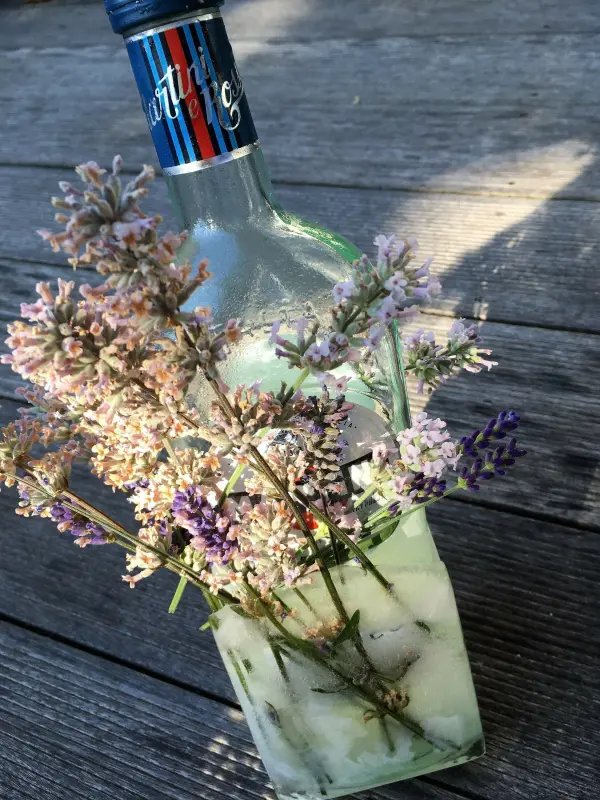 Ein Flaschenkühler aus Eis umgibt eine Flasche, die mit bunten Blumen dekoriert ist, auf einer Holzoberfläche.