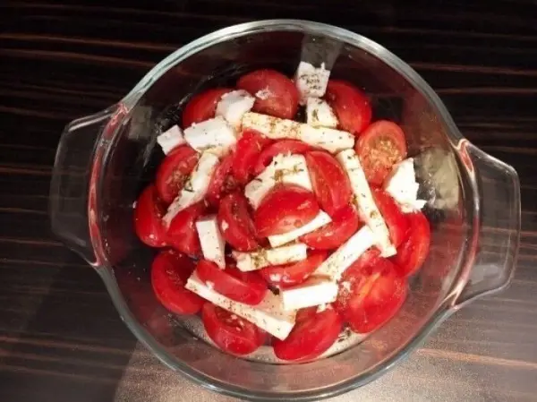 Saftige Tomaten sind in einer Glasform angeordnet und mit Feta und Kräutern garniert, bereit zum Backen als Gratin.
