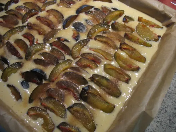 Ein geformter Obstkuchen vom Blech liegt auf einem Blech, bedeckt mit geschnittenen Obststücken in einer cremigen Masse.