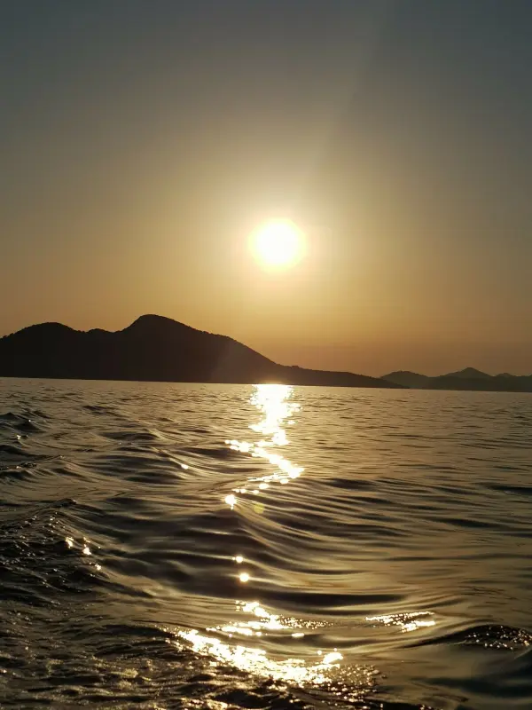 Der Sonnenuntergang spiegelt sich auf dem ruhigen Meer, während sanfte Wellen gegen das Ufer plätschern.