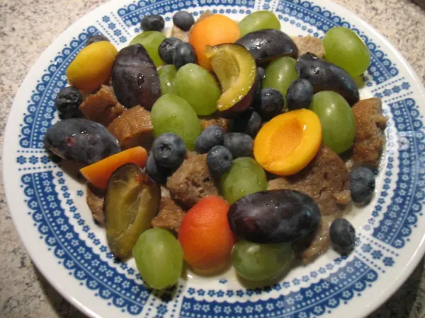 Eine farbenfrohe Milchkaltschale mit Beeren und Früchten liegt auf einem blau gemusterten Teller, umgeben von einer neutralen Tischoberfläche.