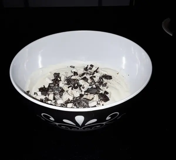 Ein Becher mit Joghurteis ist mit Schokoladenstückchen bedeckt, umgeben von einem schlichten, dunklen Hintergrund.