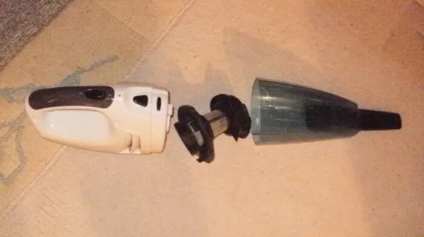 Ein Handstaubsauger liegt auseinandergebaut auf einem Teppich, die Teile zeigen den Zustand vor der Verwendung.