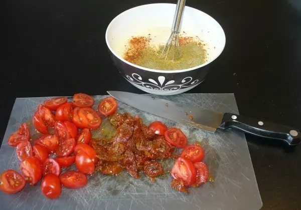 Kirschtomaten teilen und, wenn man mag, zusätzlich eingelegte Tomaten klein hacken.