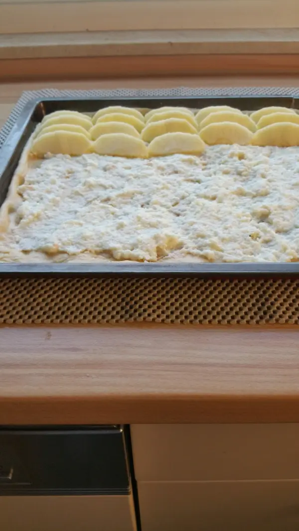 Ein Blech mit Apfelkuchen, belegt mit Streuseln und gleichmäßig geschnittenen Äpfeln, steht auf einem Holztisch.