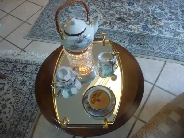 Ein Teekannen-Set steht auf einem glänzenden Tablett, umgeben von feinem Geschirr, auf einem Teppichboden in einem Wohnzimmer.