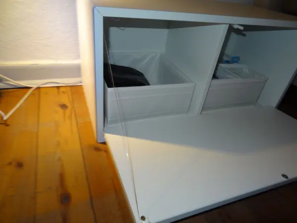Eine offene Drucktür eines Nachttischs zeigt, wie sie in einem Raum auf einem Holzboden steht und dabei auf den Boden gefallen ist.