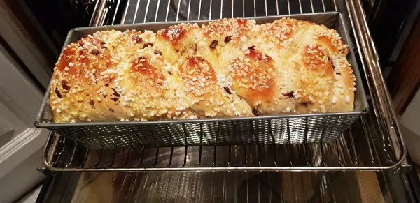 Ein goldbrauner Hefezopf mit rosinen und topfen steht frisch gebacken auf dem Rost in einem Backofen.