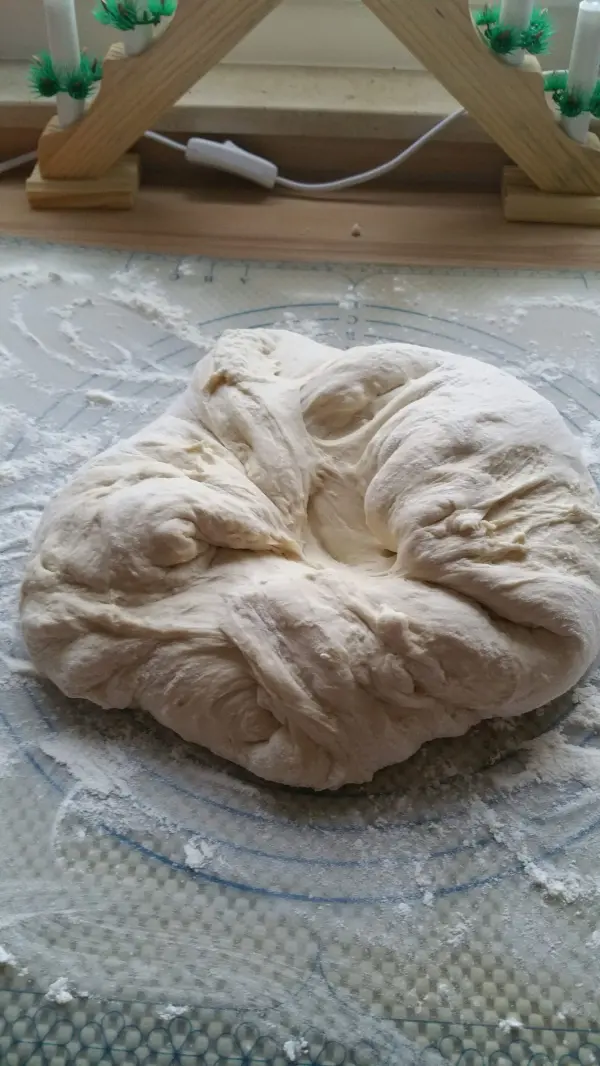 Ein runder Teigklumpen liegt auf einer bemehlten Fläche, bereit zum Formen leckerer Brötchen mit Liebe.