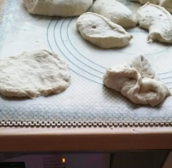 Teigstücke liegen auf einer Arbeitsfläche und warten darauf, zu leckeren Brötchen verarbeitet zu werden.