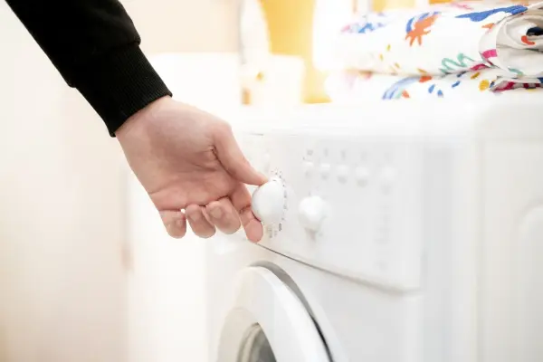 Eine Hand stellt den Waschzyklus an einer Waschmaschine ein, während der Bezug des Beddinge-Schlafsofas gewaschen wird.