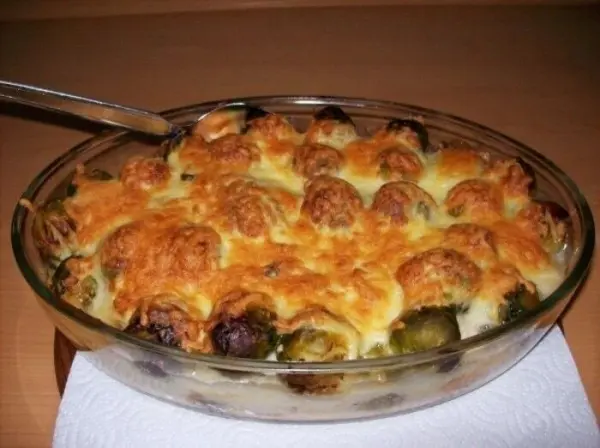 Ein Auflauf aus Rosenkohl und Hackbällchen, überbacken mit Käse, steht appetitlich in einer Glasform auf einem Tisch.