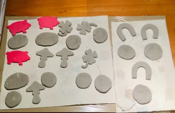 Kleine, grau gefärbte Glücksbringerformen aus Ton liegen auf einem Tisch, einige mit roten Akzenten.