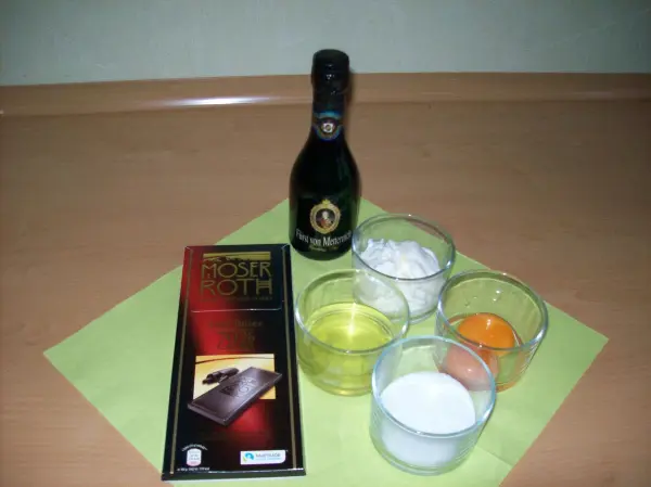 Zutaten für Mousse au Chocolat und fruchtiger Sektschaum auf einem Tisch: Schokolade, Sekt, Ei, Zucker und Sahne in Gläsern.