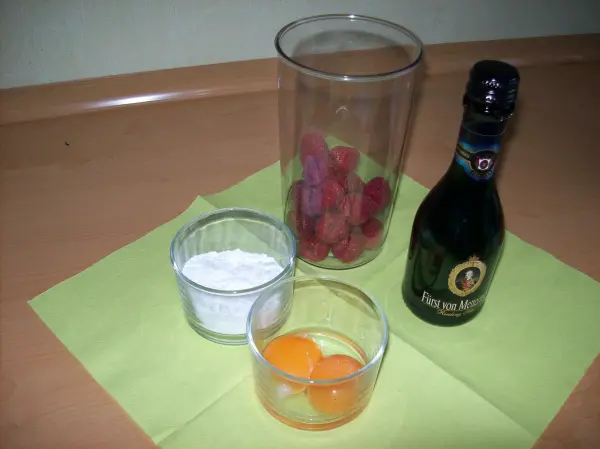 Gläser mit Eiern, Zucker und Sekt sowie frischen Beeren liegen auf einer grünen Serviette in einer hellen Umgebung.
