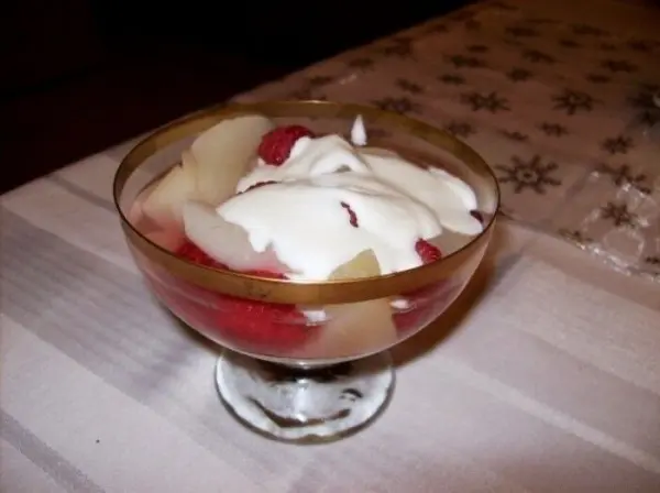 Eingelegte Birnen liegen zusammen mit frischen Himbeeren und Sahne in einem Glas auf einem dekorativen Tisch.