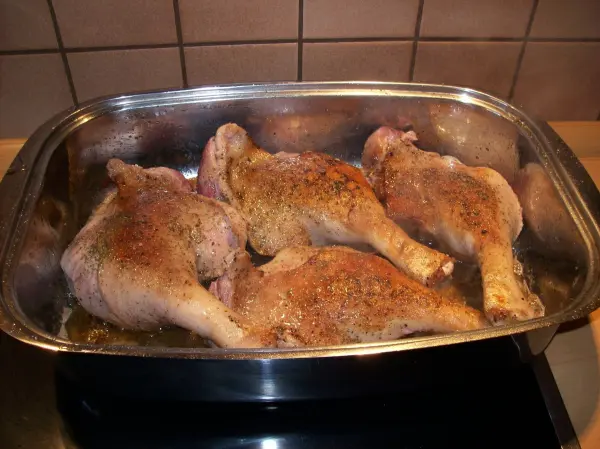 Gänsekeulen braten in einer Auflaufform, umgeben von einer dunklen Rotweinsoße auf dem Herd in einer Küche.