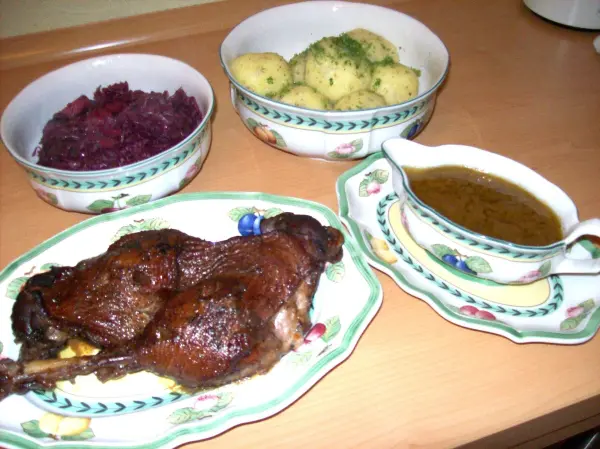 Saftige Gänsekeulen in Rotweinsoße garnieren einen Tisch, umgeben von Beilagen wie Kartoffeln und Rotkohl.