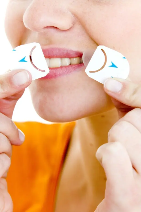 Eine Frau hält zwei kleine Aufkleber an ihren Lippen, um Herpes zu behandeln, während sie in einem hellen Raum steht.