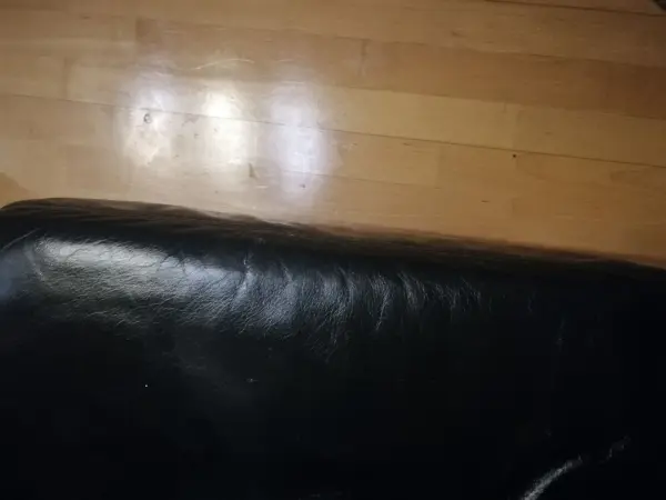 Eine schwarze Lederoberfläche liegt neben einem glänzenden Parkettboden, auf dem möglicherweise Eddingflecken sichtbar sind.