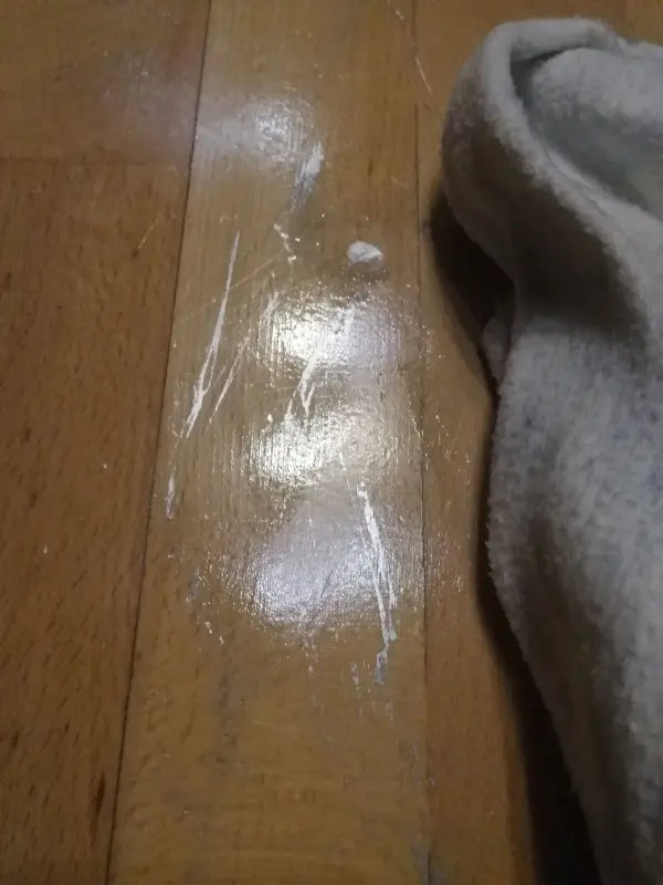 Ein Reinigungstuch entfernt Edding-Spuren von einem Parkettboden, während eine Holzoberfläche im Hintergrund sichtbar ist.