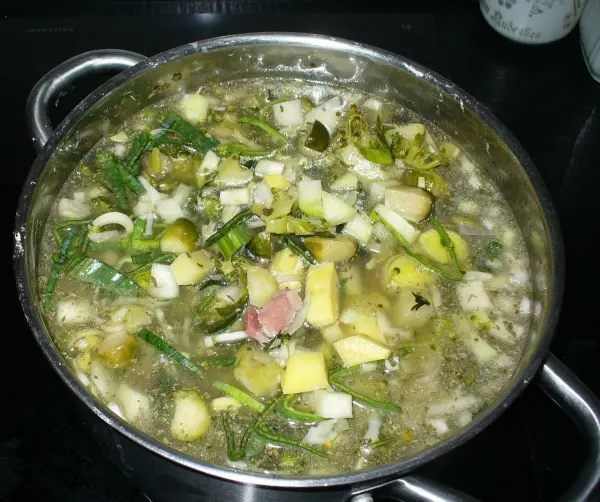 Ein großer Topf mit Graupensuppe, gefüllt mit buntem Gemüse, köchelt auf dem Herd in einer modernen Küche.