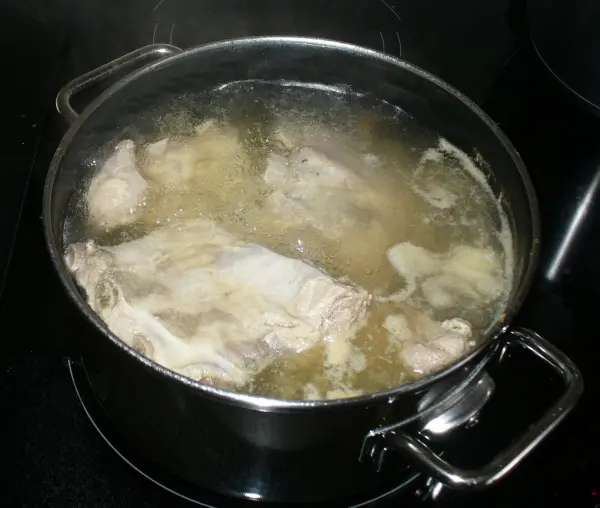 In einem Topf kocht eine Brühe mit Fleischstücken, die auf einem Herd zubereitet wird, um eine herzhafte Graupensuppe zu kreieren.