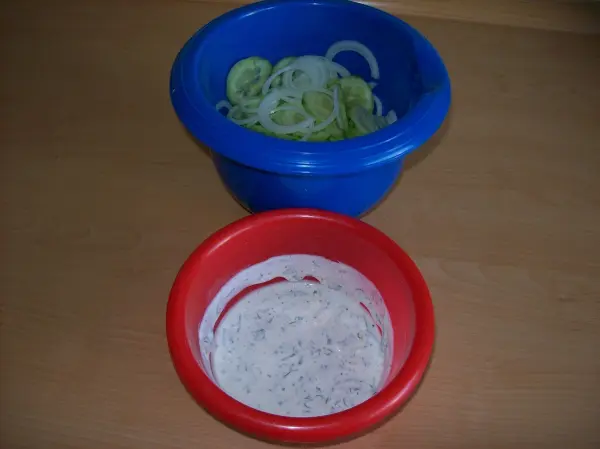 Gedünsteter Seelachs liegt in einem roten Schälchen mit frischer Kräutersoße, während frische Zutaten in einem blauen Schälchen liegen.