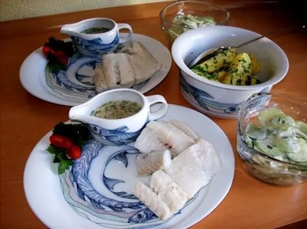 Zwei Teller mit gedünstetem Seelachs, frisch zubereiteter Kräutersoße und Beilagen, schön angerichtet auf einem Holztisch.