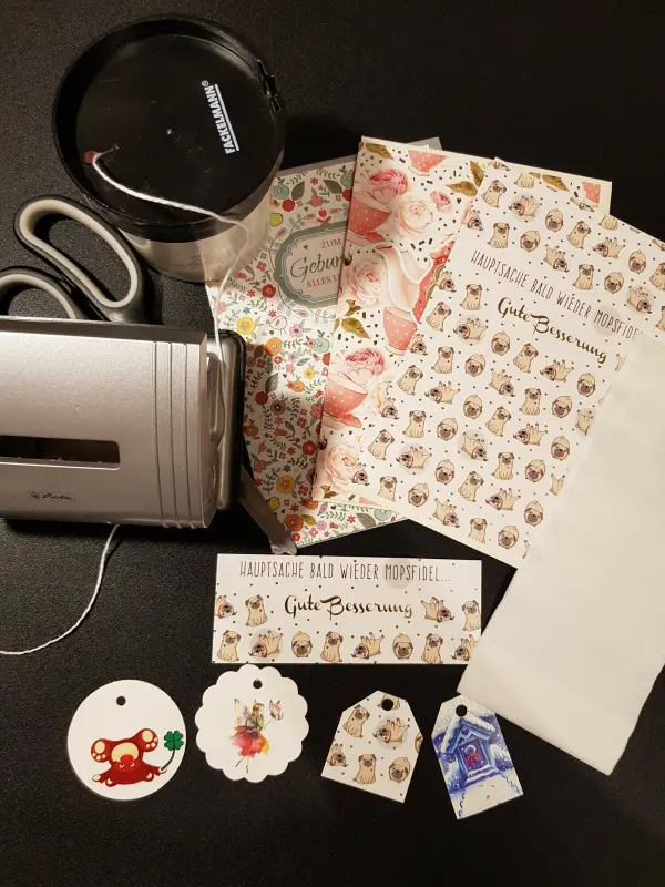 Schöne Teebeutel werden mit buntem Geschenkpapier und Anhängern vorbereitet. Die Umgebung ist eine dunkle Tischoberfläche.